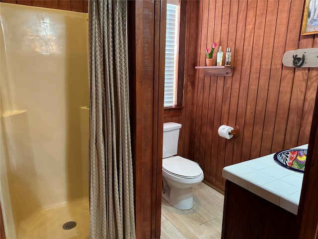 bathroom with a shower with shower curtain, wooden walls, toilet, and vanity