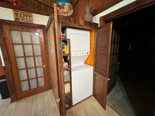 laundry area featuring wood walls, light hardwood / wood-style floors, and stacked washer and dryer