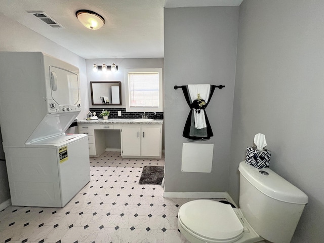 bathroom with visible vents, toilet, stacked washer and dryer, decorative backsplash, and tile patterned floors