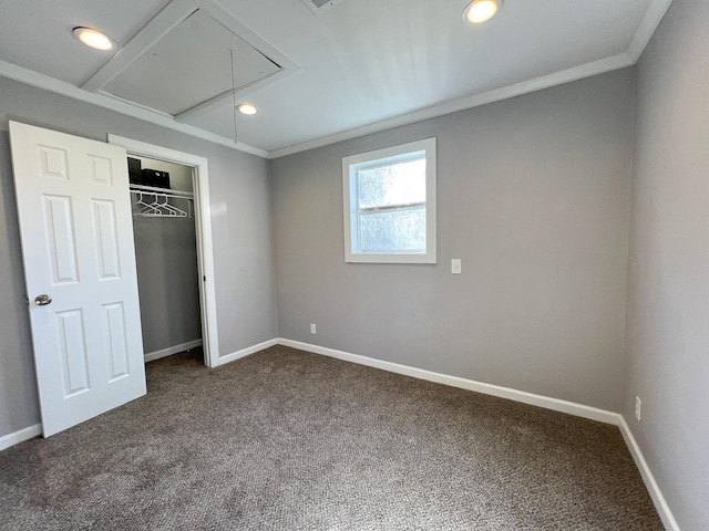 unfurnished bedroom with ornamental molding, attic access, baseboards, and dark colored carpet