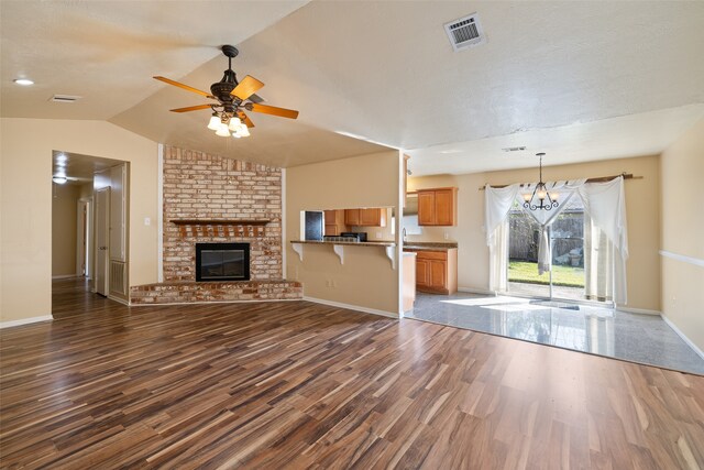 unfurnished living room featuring dark hardwood / wood-style flooring, a fireplace, vaulted ceiling, and ceiling fan with notable chandelier