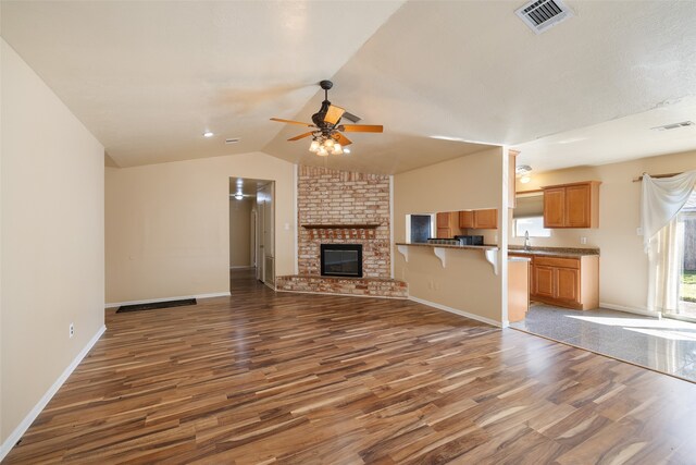 unfurnished living room with sink, ceiling fan, a fireplace, dark wood-type flooring, and vaulted ceiling