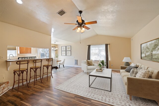 living room with dark wood-type flooring, lofted ceiling, a textured ceiling, and ceiling fan with notable chandelier