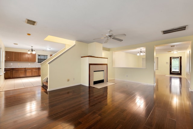 unfurnished living room with a tiled fireplace, hardwood / wood-style floors, and ceiling fan with notable chandelier