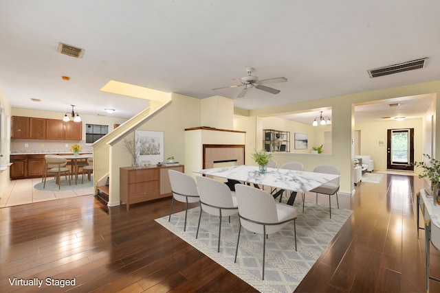 dining area with hardwood / wood-style flooring, ceiling fan with notable chandelier, and a tile fireplace