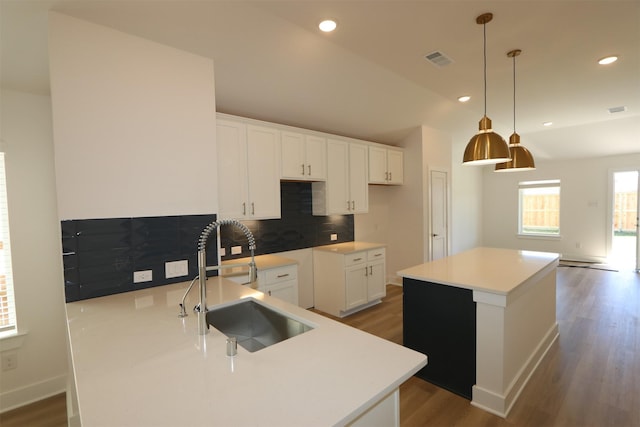 kitchen featuring visible vents, a sink, wood finished floors, a center island, and decorative backsplash