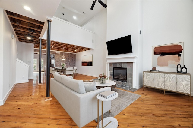 living room featuring hardwood / wood-style flooring, brick wall, a towering ceiling, a fireplace, and ceiling fan