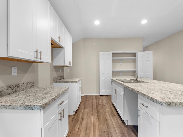 kitchen with white cabinetry, sink, light hardwood / wood-style floors, and a kitchen island with sink