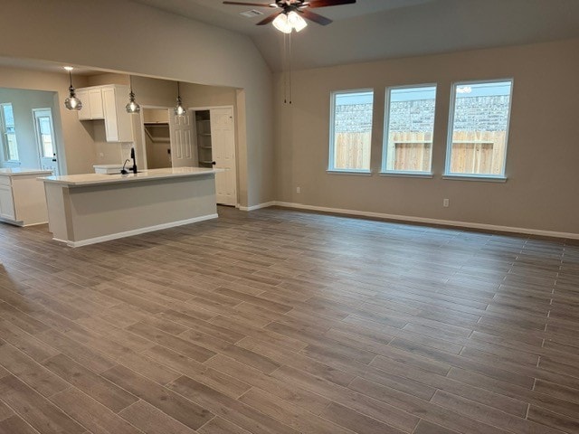 unfurnished living room with a wealth of natural light, hardwood / wood-style flooring, vaulted ceiling, and ceiling fan