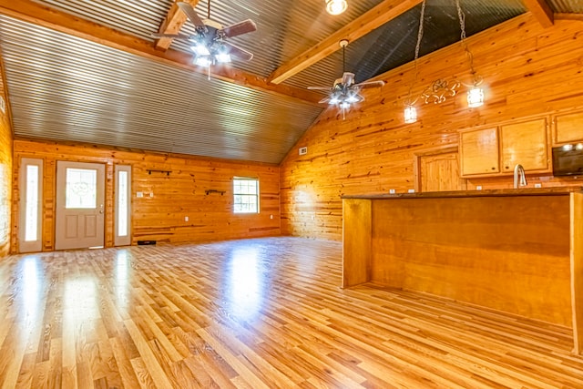 unfurnished living room with light wood-type flooring, plenty of natural light, wooden walls, and beamed ceiling