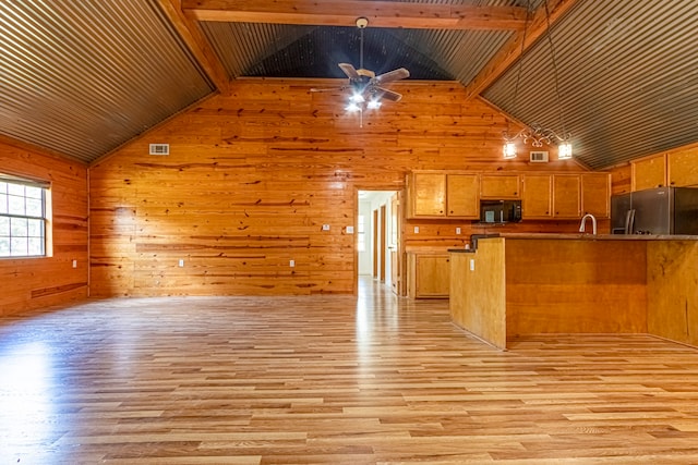 kitchen with light wood-type flooring, stainless steel refrigerator, wood walls, beamed ceiling, and kitchen peninsula