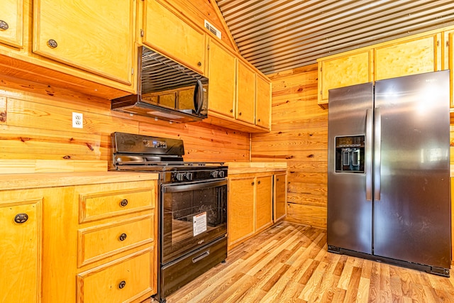 kitchen with black appliances, wooden walls, vaulted ceiling, and light hardwood / wood-style flooring