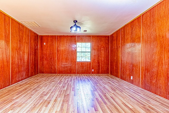 unfurnished room with light hardwood / wood-style flooring and wooden walls