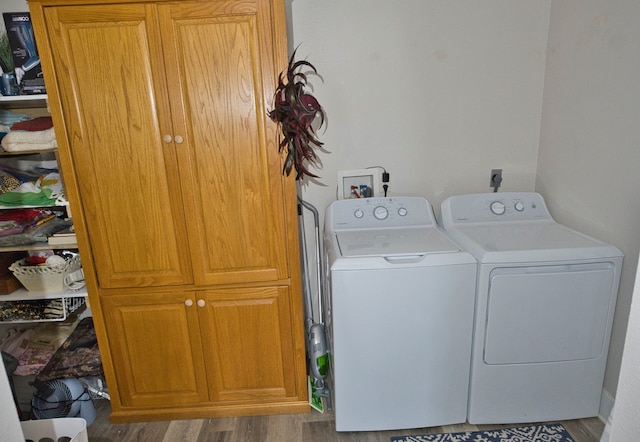 clothes washing area featuring hardwood / wood-style flooring, washing machine and dryer, and cabinets