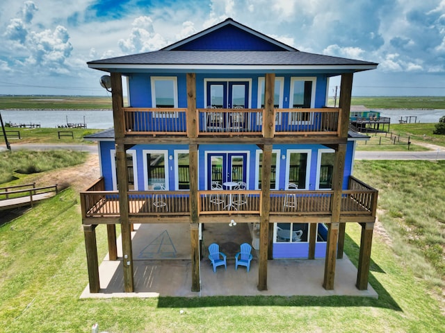 rear view of house featuring a water view, a lawn, and a patio