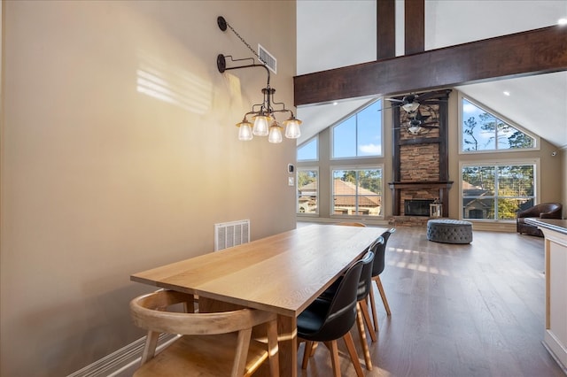 dining room with a stone fireplace, plenty of natural light, high vaulted ceiling, and hardwood / wood-style flooring