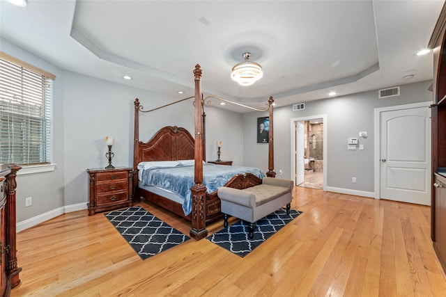 bedroom featuring ensuite bath, wood-type flooring, and a tray ceiling