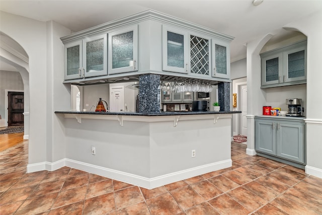 kitchen featuring a kitchen bar, kitchen peninsula, gray cabinets, and dark stone countertops