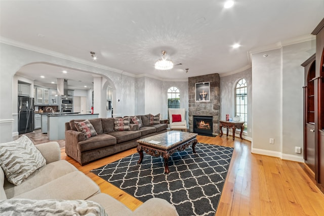 living room featuring a stone fireplace, light wood-type flooring, ornamental molding, and sink