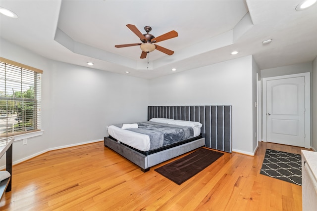 bedroom with light hardwood / wood-style flooring, ceiling fan, and a tray ceiling