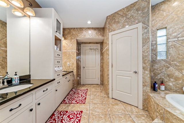 bathroom featuring tile walls, vanity, tiled tub, and tile patterned floors