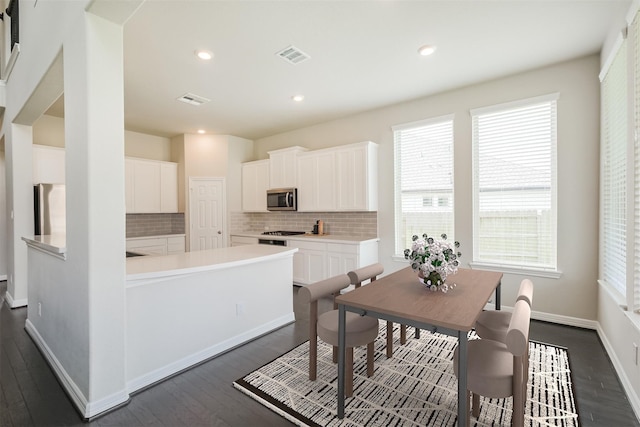 kitchen with stainless steel appliances, white cabinetry, backsplash, and dark hardwood / wood-style flooring