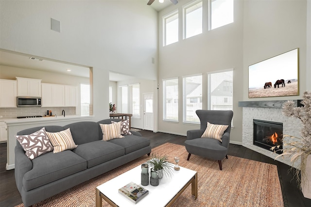 living room featuring dark wood-type flooring, ceiling fan, a high ceiling, and a fireplace