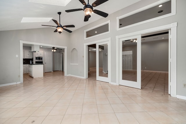 empty room with lofted ceiling with skylight, french doors, light tile patterned floors, and ceiling fan