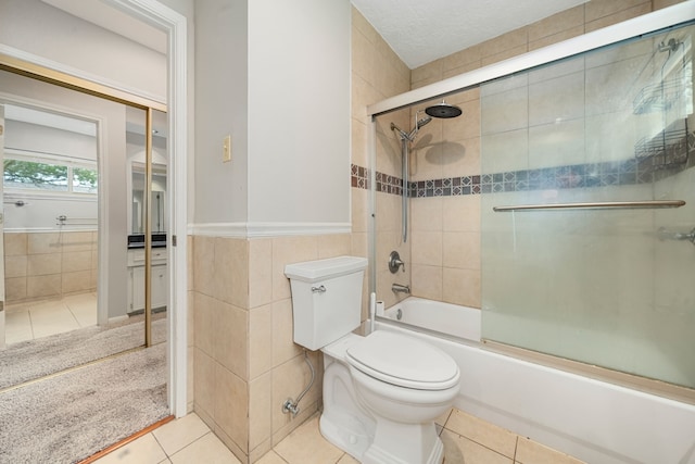 bathroom with toilet, tile patterned floors, tile walls, and bath / shower combo with glass door