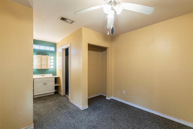 unfurnished bedroom featuring dark colored carpet, ceiling fan, and ensuite bathroom