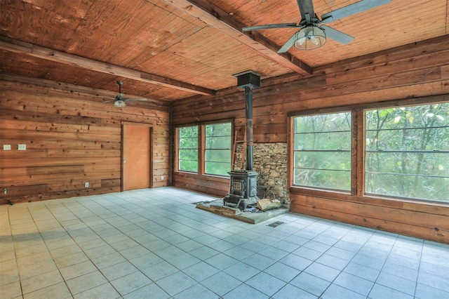 unfurnished living room featuring a wood stove, light tile patterned floors, beam ceiling, wooden walls, and wood ceiling