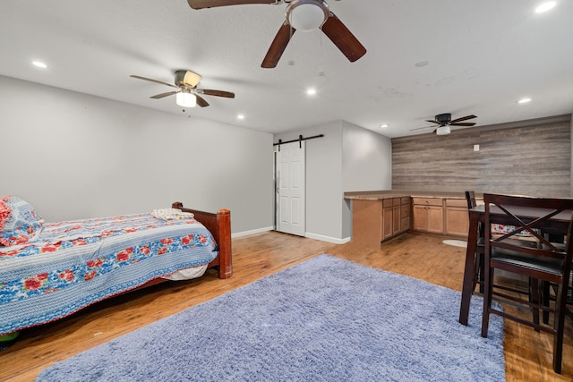 bedroom featuring light hardwood / wood-style floors, a barn door, and ceiling fan