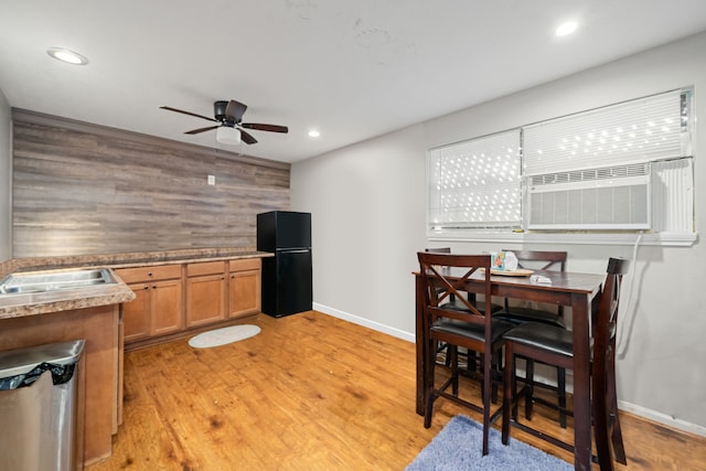 kitchen featuring black fridge, light hardwood / wood-style floors, wood walls, sink, and ceiling fan