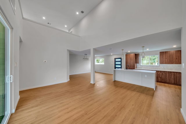 unfurnished living room featuring light wood-type flooring, a towering ceiling, and sink