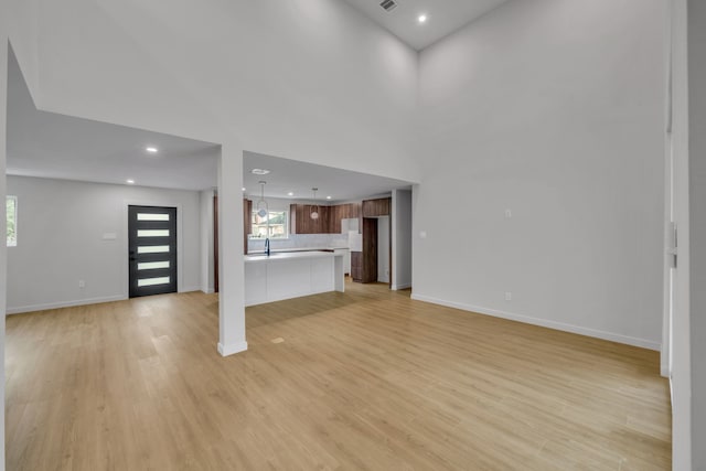 unfurnished living room with sink, a towering ceiling, and light wood-type flooring