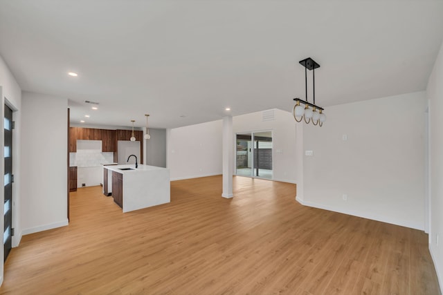 unfurnished living room with light wood-type flooring, an inviting chandelier, and sink