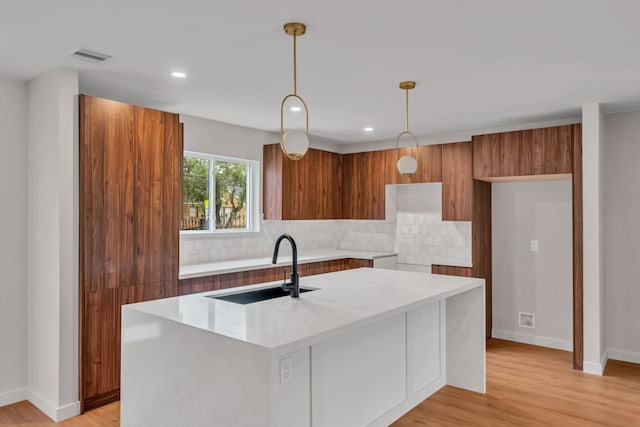 kitchen with tasteful backsplash, a kitchen island with sink, light hardwood / wood-style flooring, and sink