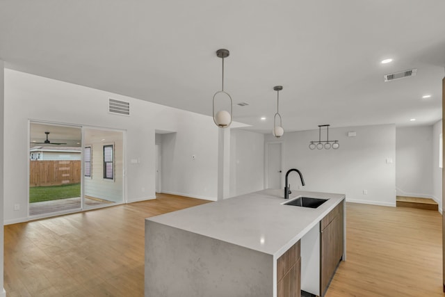 kitchen featuring sink, light hardwood / wood-style flooring, ceiling fan, an island with sink, and decorative light fixtures