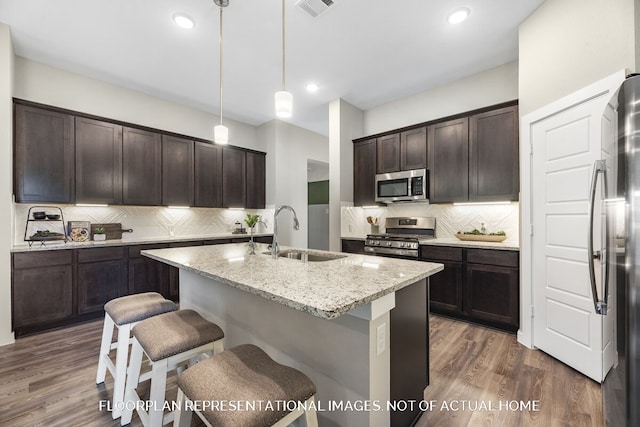 kitchen with stainless steel appliances, pendant lighting, sink, dark wood-type flooring, and a kitchen island with sink