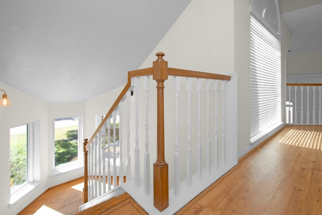 stairway with a wealth of natural light, wood-type flooring, and lofted ceiling