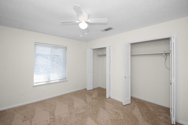 unfurnished bedroom featuring multiple closets, light colored carpet, and ceiling fan