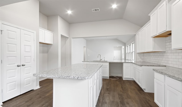 kitchen featuring dark wood-type flooring, white cabinets, vaulted ceiling, and a center island