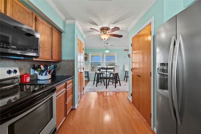 kitchen featuring dark stone counters, hanging light fixtures, crown molding, light hardwood / wood-style flooring, and appliances with stainless steel finishes