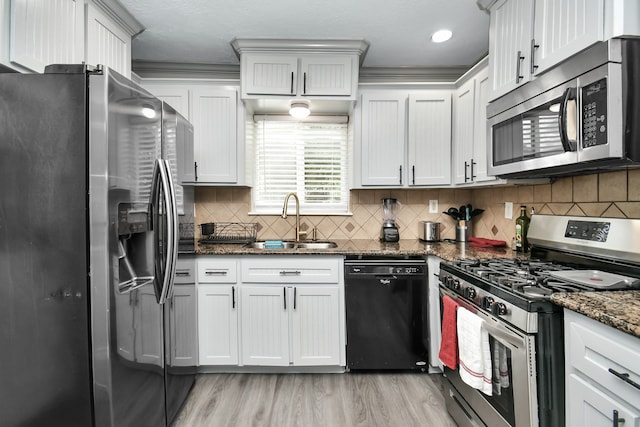 kitchen with appliances with stainless steel finishes, white cabinetry, dark stone countertops, sink, and crown molding