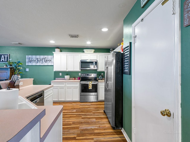 kitchen featuring white cabinetry, light wood-type flooring, appliances with stainless steel finishes, and a textured ceiling