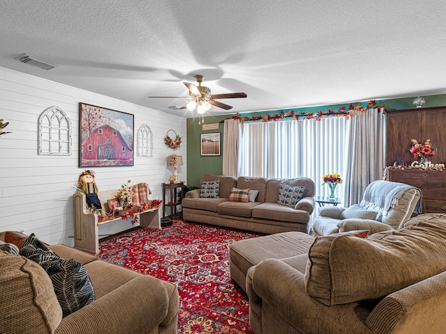 carpeted living room with wood walls, a textured ceiling, and ceiling fan