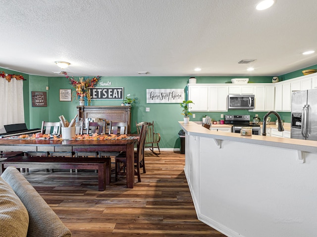 kitchen featuring stainless steel appliances, a breakfast bar, a textured ceiling, white cabinets, and dark wood-type flooring