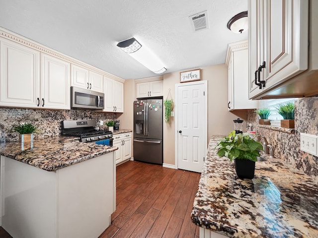 kitchen with white cabinetry, appliances with stainless steel finishes, dark hardwood / wood-style floors, dark stone countertops, and backsplash