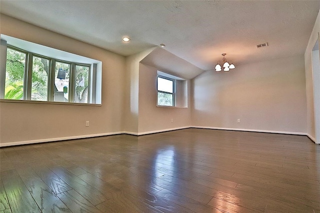 empty room featuring dark hardwood / wood-style flooring, a textured ceiling, and a notable chandelier