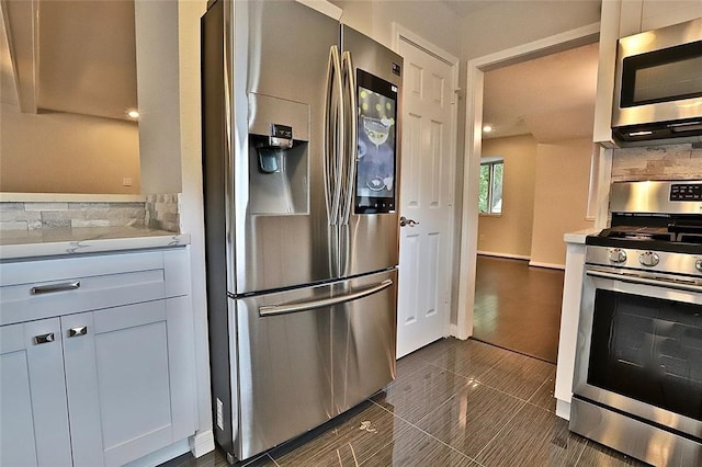 kitchen featuring white cabinets, appliances with stainless steel finishes, dark tile patterned flooring, and backsplash